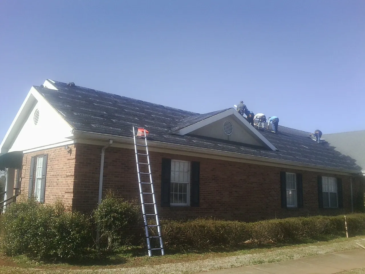 Crew tearing shingles off a brick ranch roof with a ladder set — Emergency Roof Repair work by our crew in Brookings