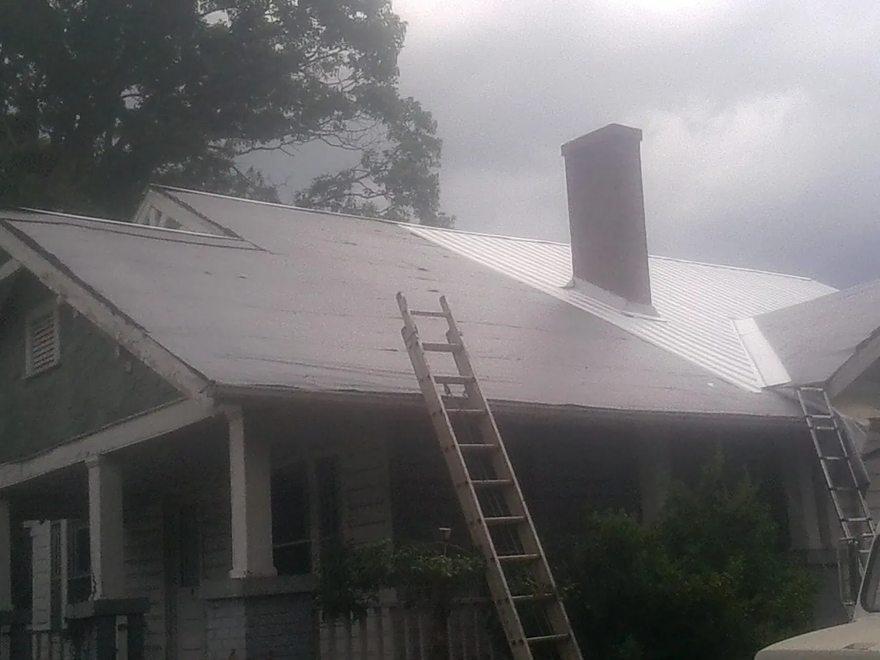 Ladders against a metal roof on an older home with a brick chimney in Brookings