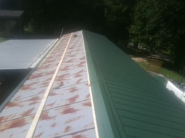 Old rusted panels beside newly installed green metal roofing — Wind Damage Roof Repair by Roofing Brothers in Brookings