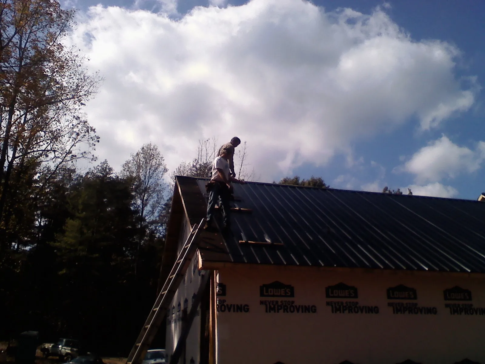 Roofer fastening dark metal panels high against a cloudy sky, from a Roof Inspection job in Brookings